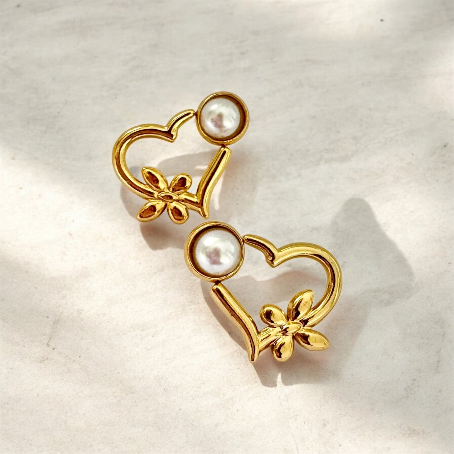 Gold heart-shaped earrings with pearls on a light background